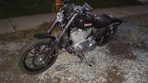 1988 Ford Bronco - Black Harley-Davidson motorcycle parked on gravel with a sidewalk in the background.
