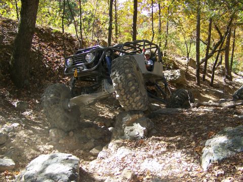 1992 Jeep YJ - Custom off-road buggy with roll cage navigating a rocky trail in a wooded area.