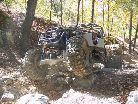 1992 Jeep YJ - This heavily modified off-road vehicle navigates a rocky incline in a wooded area.