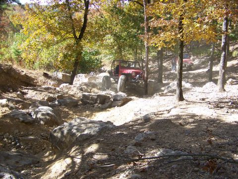 1992 Jeep YJ - A red 1992 Jeep YJ tackles a challenging off-road course amidst autumn foliage, with another Jeep visible in the background.