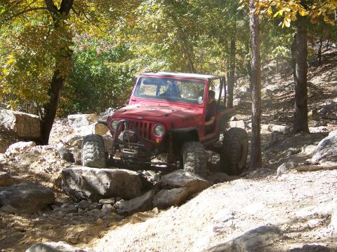 1992 Jeep YJ - A red Jeep Wrangler TJ is shown off-roading over large rocks on a sunny day.