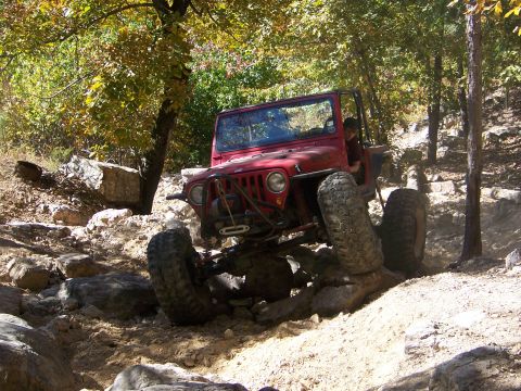 1992 Jeep YJ - A red 1992 Jeep YJ tackles a challenging off-road trail with steep inclines and large rocks.