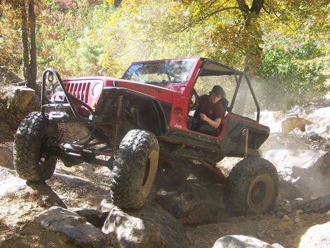 1992 Jeep YJ - A red 1992 Jeep YJ navigates a rocky trail with a driver at the wheel.