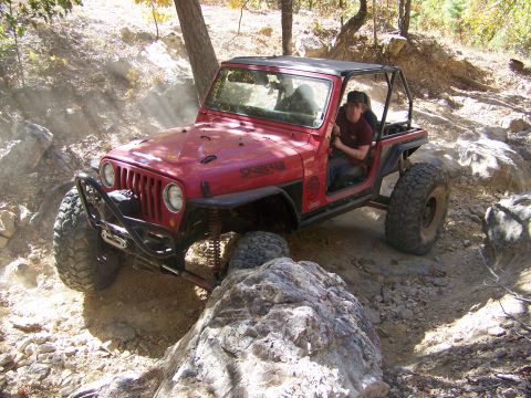 1992 Jeep YJ - A red Jeep Wrangler is shown off-roading on a challenging rocky trail.