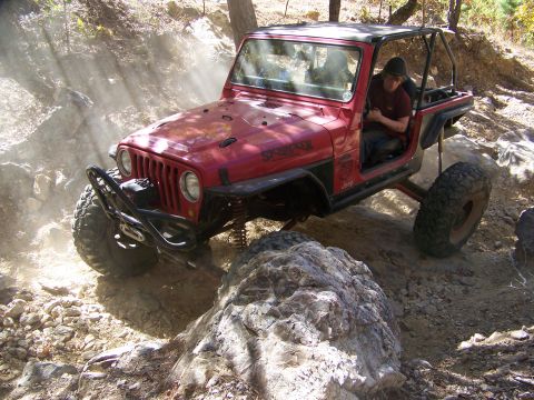 1992 Jeep YJ - A red 1992 Jeep YJ navigates a rocky trail, kicking up dust.