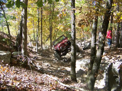 1992 Jeep YJ - Red 1992 Jeep YJ navigating a challenging rocky terrain in a forest during autumn.