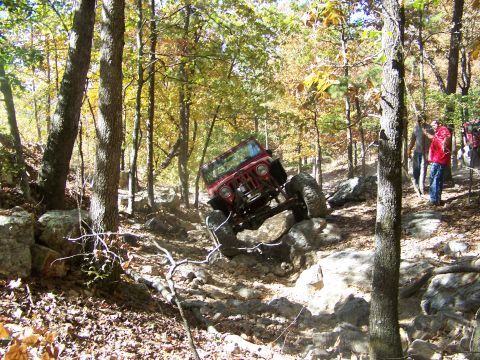 1992 Jeep YJ - A red Jeep navigates a rocky trail in a forest setting with onlookers present.