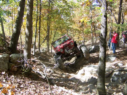 1992 Jeep YJ - A red 1992 Jeep YJ tackles a challenging off-road course amidst autumn foliage.