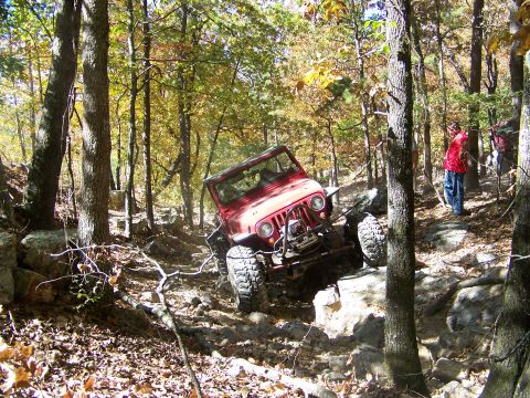 1992 Jeep YJ - A red 1992 Jeep YJ tackles a challenging off-road course amidst trees with fall foliage.