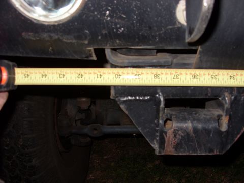 1988 Ford Bronco - A tape measure is used to gauge the distance across a vehicle's frame, showing suspension and tire details.