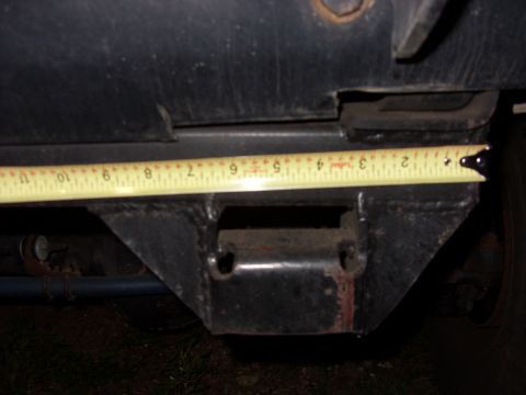 1988 Ford Bronco - A yellow tape measure stretched horizontally under the black rear bumper and body of a truck, checking clearance or spacing against a welde…