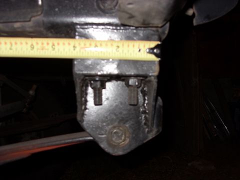 1988 Ford Bronco - Close-up under a truck of a black-painted leaf spring shackle hanger bracket with two protruding threaded studs and a large hex bolt, with…