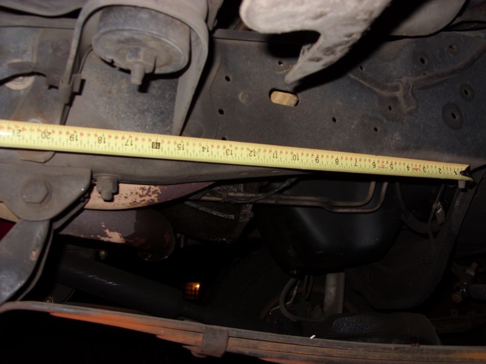 Close-up of vehicle frame and suspension parts with a yellow tape measure laid across it