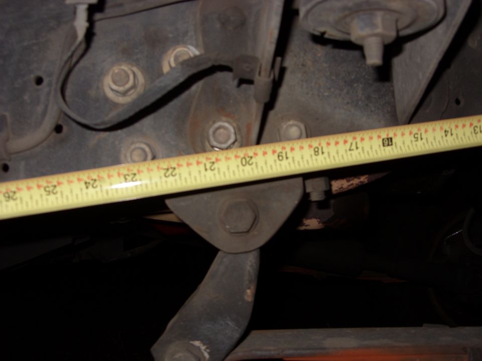 Close-up of vehicle suspension parts with a yellow measuring tape showing measurements from 13 to 26 inches