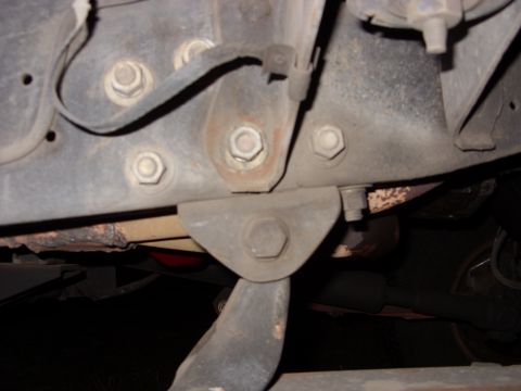 1988 Ford Bronco - Tight underbody close-up of a truck frame rail and crossmember area, showing several large hex-head bolts through a reinforcement plate, a…
