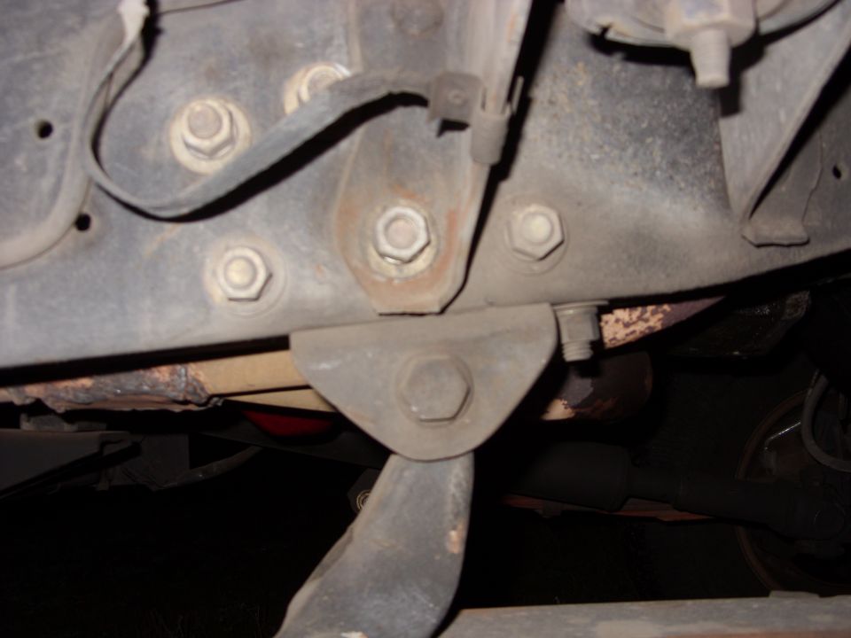 Underbody close-up of truck frame bracket with large hex bolts and brake line