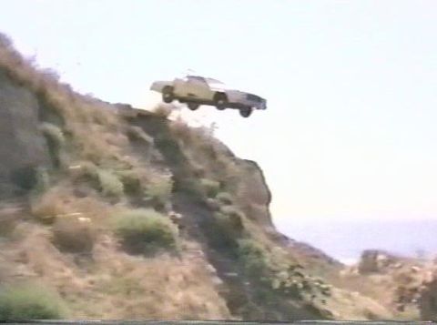 2003 Ford Crown Victoria - A car is captured in mid-air as it drives off a cliffside road.