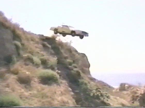 Car mid-air, jumping off a cliff with ocean in background