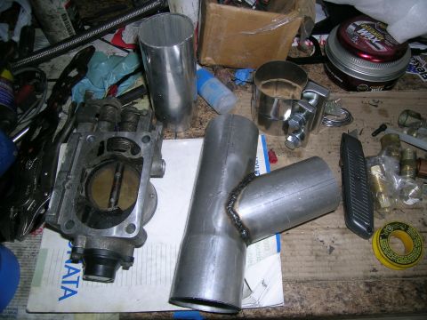 1995 Ford Probe - Various automotive parts, including a throttle body and custom exhaust components, are laid out on a cluttered workbench.