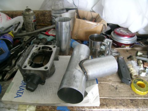 1995 Ford Probe - A throttle body and custom exhaust piping are laid out on a workbench, suggesting a turbo build project.