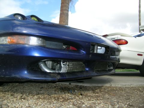 1995 Ford Probe - Close-up of a blue car's front end, showing an aftermarket intercooler and piping, with another car visible behind it.