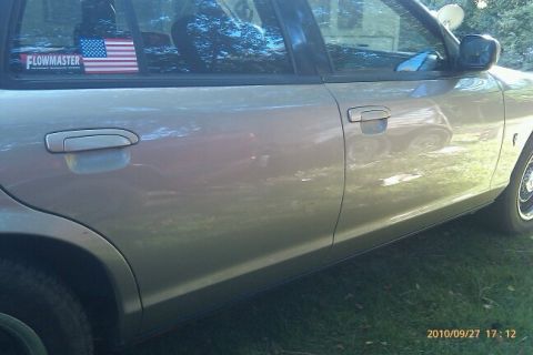 2000 Mercury Grand Marquis - Side view of a tan sedan showing the door panel and a sticker on the rear window.