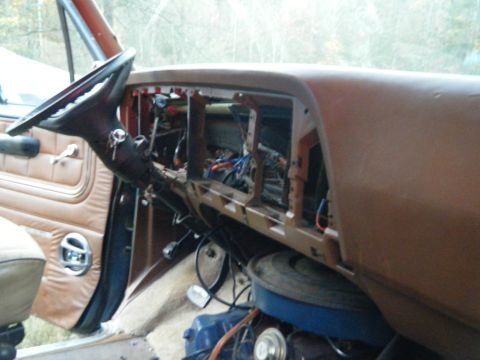1981 Ford E350 - The dashboard of a vehicle is disassembled, revealing wiring and internal components. The steering wheel and part of the door are visible.