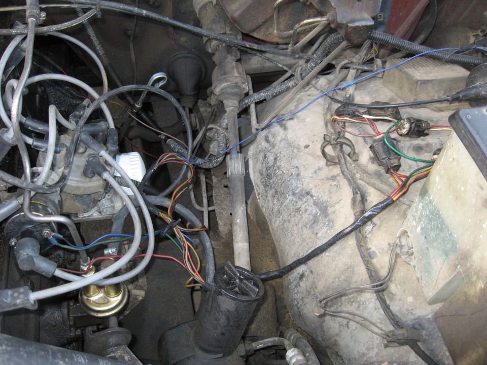 Grimy engine bay with white plug wires, distributor, gold fuel pump and loose wiring harness