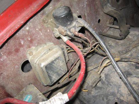 1981 Ford Bronco - Dusty inner fender detail showing a fender-mounted ignition coil on its bracket and a boxy voltage regulator bolted to the faded red sheet…