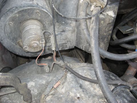1981 Ford Bronco - Grimy underhood close-up of a dust-covered brake booster and master cylinder area with a small inline component wired by an orange pigtail…