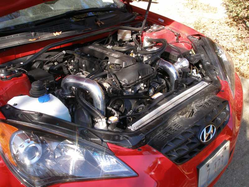 Polished intercooler piping in the engine bay of a red Hyundai coupe with hood open