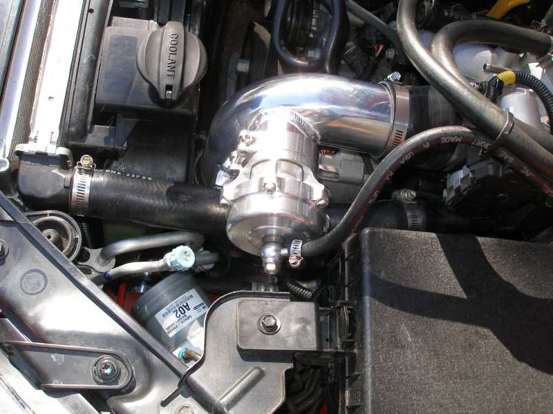 Engine bay with shiny metal pipes and a blow-off valve. Coolant reservoir cap visible
