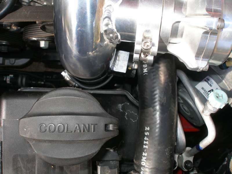 Engine bay with a black coolant cap, silver intake pipe, and black hose with white text