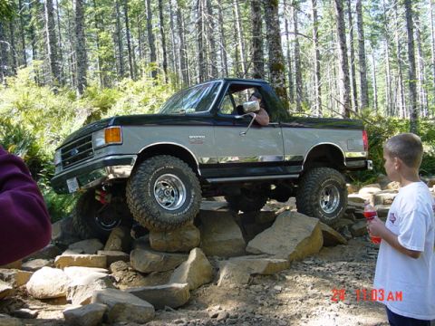 1989 Ford Bronco - This two-tone Ford Bronco is navigating a rocky obstacle on a forest trail.