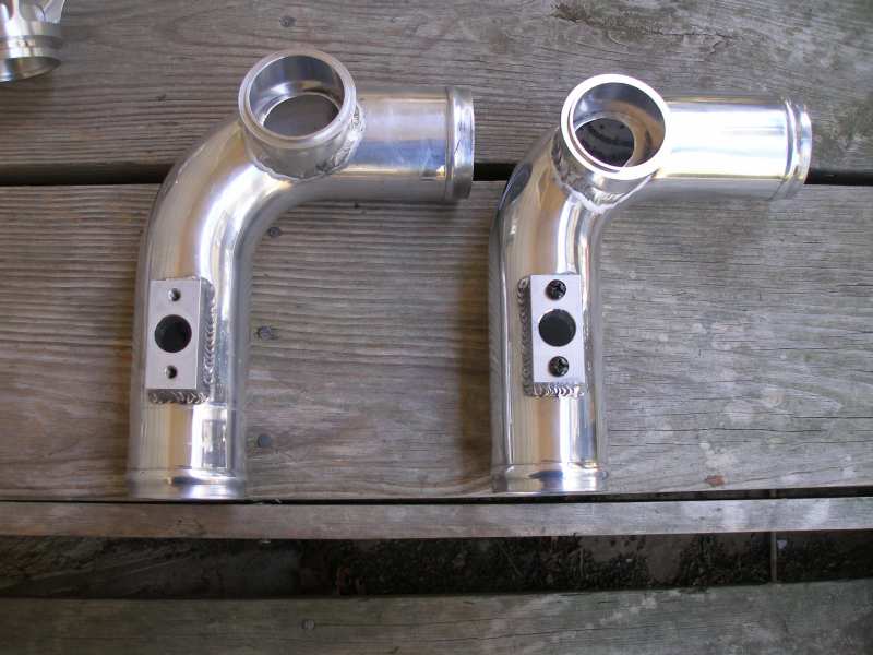 Two shiny aluminum intake pipes with sensor ports are laid out on a wooden surface