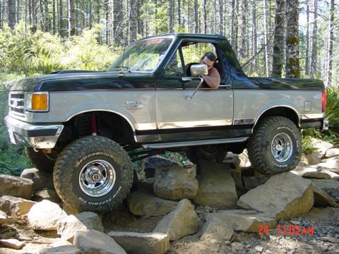1989 Ford Bronco - A modified Ford Bronco traverses a rocky trail in a wooded area.