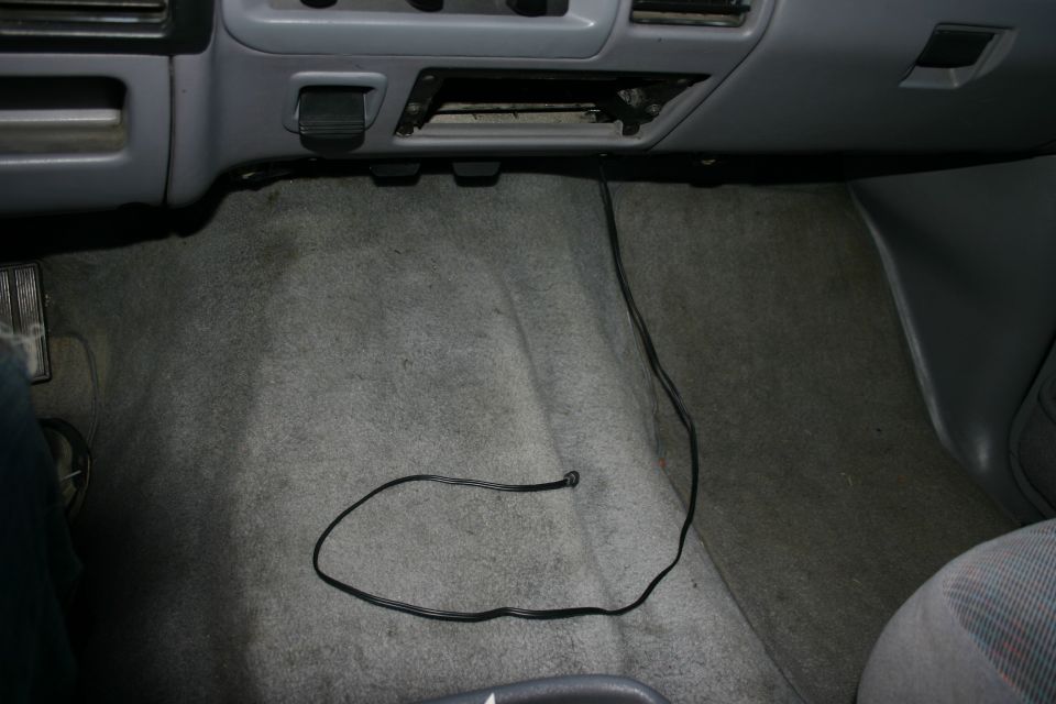 Gray vehicle floorboard with a thin cable lying on the carpet
