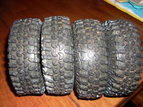 1994 Ford Escort - Four off-road tires with aggressive tread patterns are displayed on a wooden surface.
