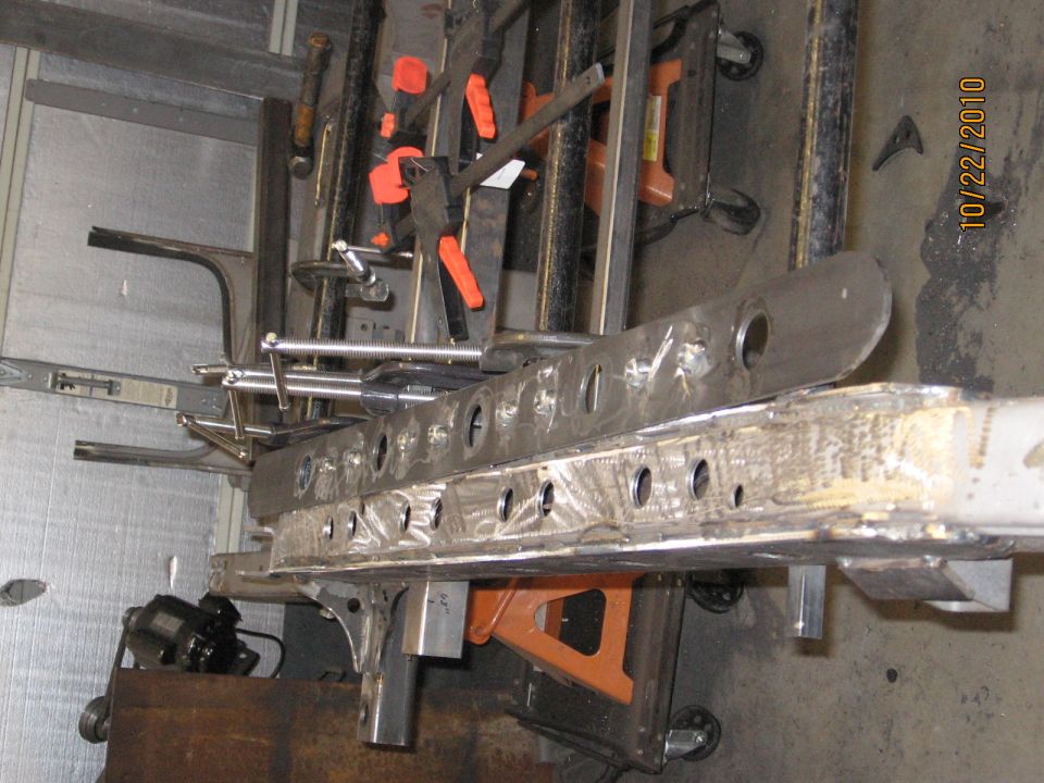 Metal frame section with numerous holes, held by orange and black clamps