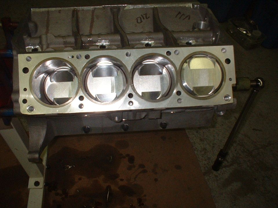 Engine block with four pistons installed, a torque wrench is visible to the right