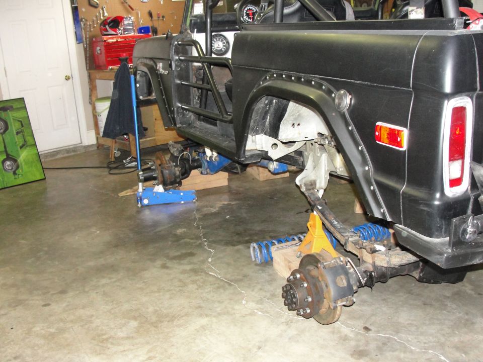 Black Ford Bronco body on jack stands with suspension removed, showing heavy-duty axles and roll cage