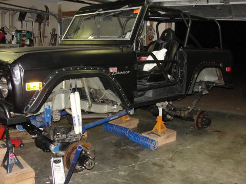 1967 Ford Mustang - This black Ford Bronco is in a garage, lifted on jack stands with its suspension components exposed for work.