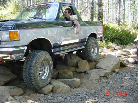 1989 Ford Bronco - This lifted Ford Bronco is shown navigating a challenging rocky trail, demonstrating its off-road capabilities.