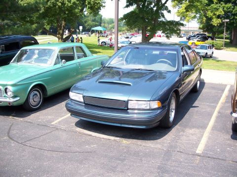 1971 Ford Ranchero - A blue sedan with a hood scoop is parked in a lot next to a green vintage car.