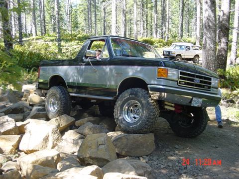 1989 Ford Bronco - A lifted Ford Bronco navigates a rocky trail with another Bronco visible in the background.