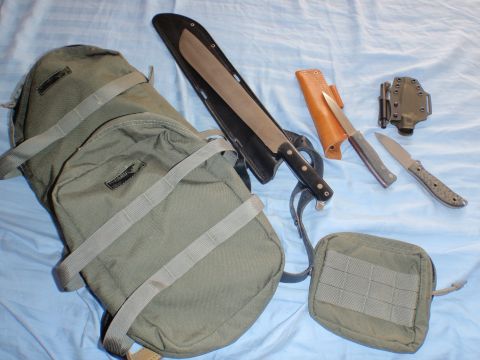 1991 Ford Bronco - A collection of outdoor gear including a backpack, a large machete, two smaller knives, and a utility pouch are laid out on a blue surface.