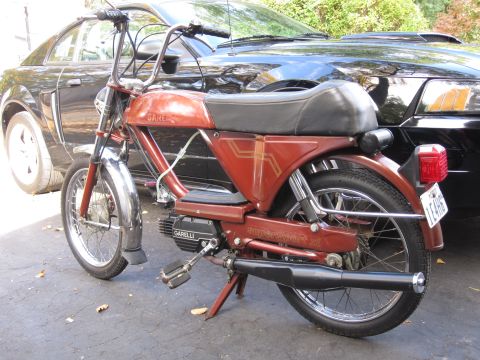 1981 Garelli Rally Sport - A red Garelli moped is parked in front of a black car. The moped has chrome fenders and a black seat.