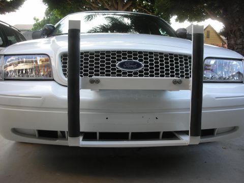 2004 Ford Crown Victoria - Head-on view of a white Ford sedan fitted with a white push bumper with black rubber-wrapped uprights bolted across the front bumper cover.…