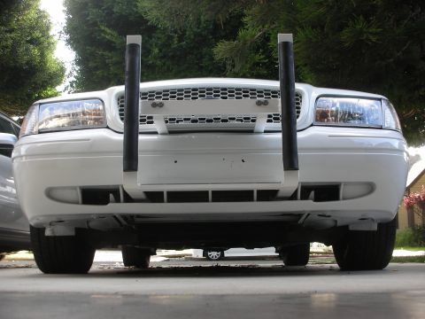 2004 Ford Crown Victoria - Low ground-level head-on view of a white Ford Crown Victoria sedan with a white push bumper bolted to the front, its two vertical uprights…