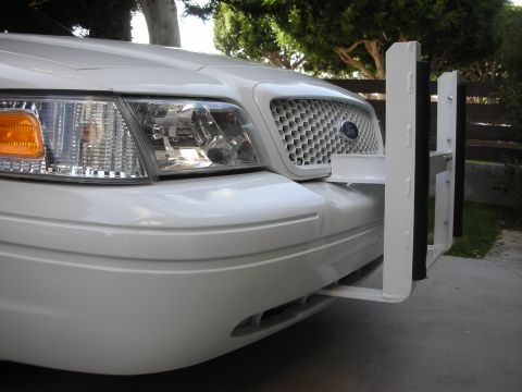 2004 Ford Crown Victoria - Close three-quarter front view of a white Ford sedan's nose, showing the clear headlight with amber corner lens, honeycomb grille with blue…